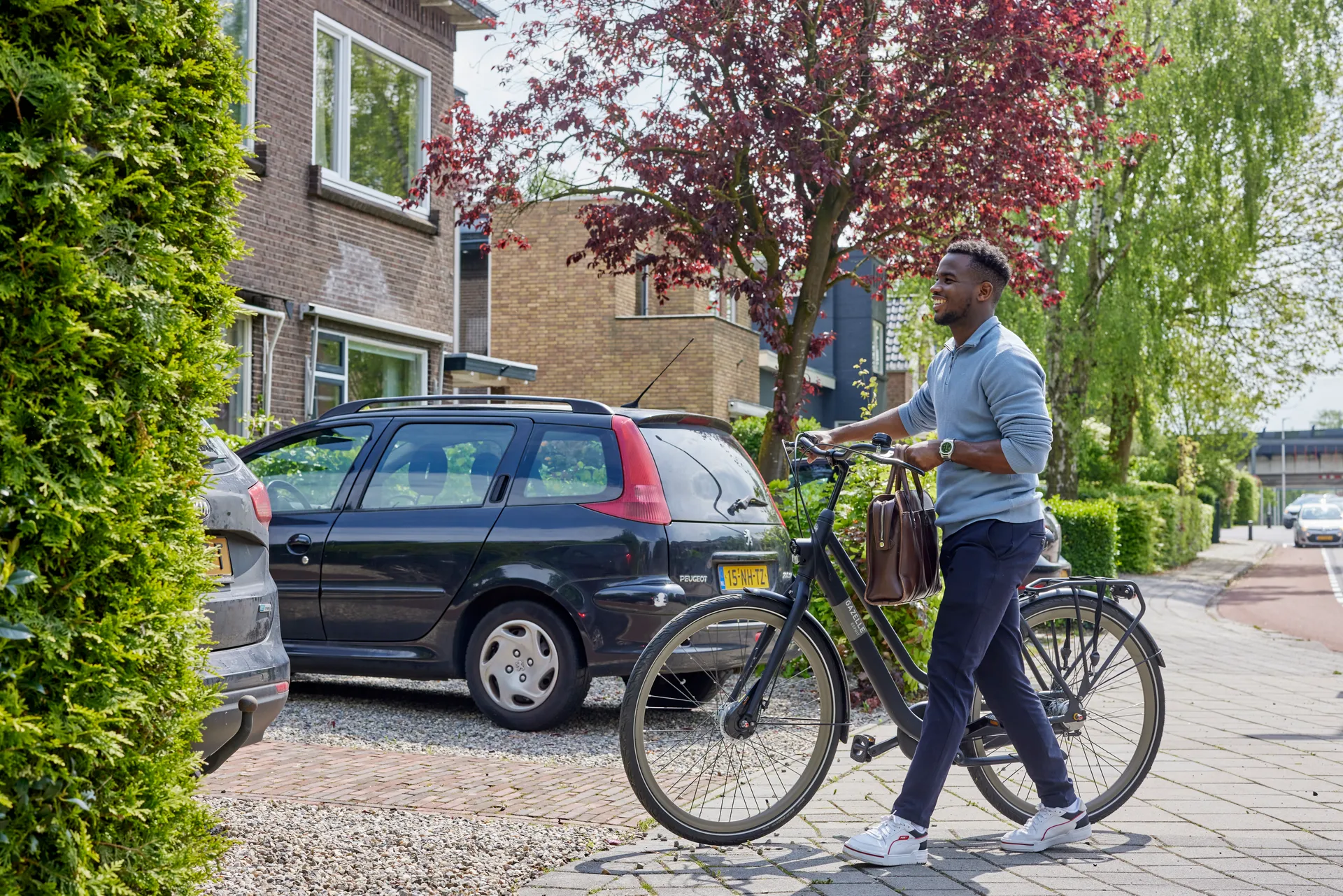 Een man die met de fiets aan zijn hand de oprit van zijn huis op loopt.
