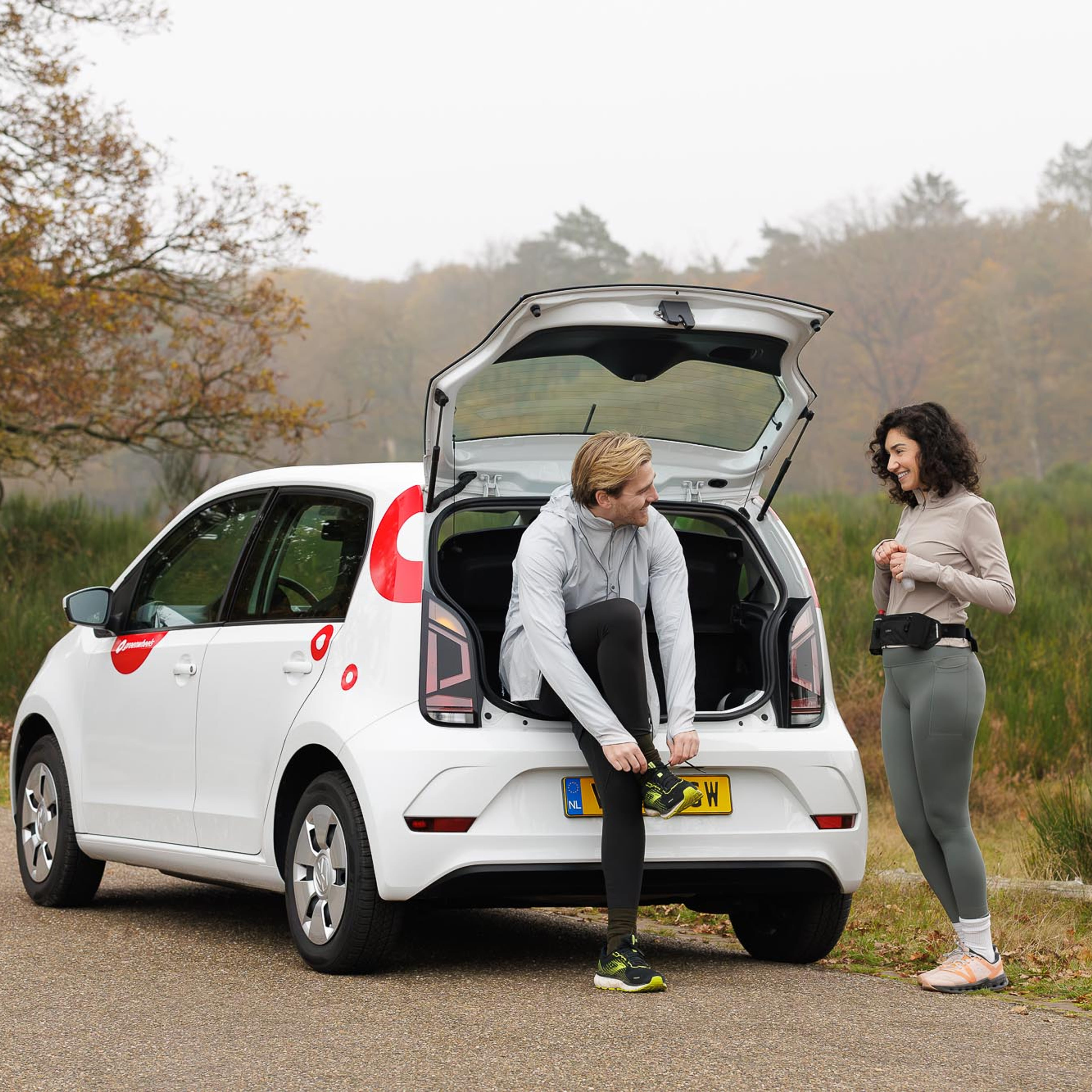 Greenwheels auto met twee mensen ervoor die gaan hardlopen in de natuur