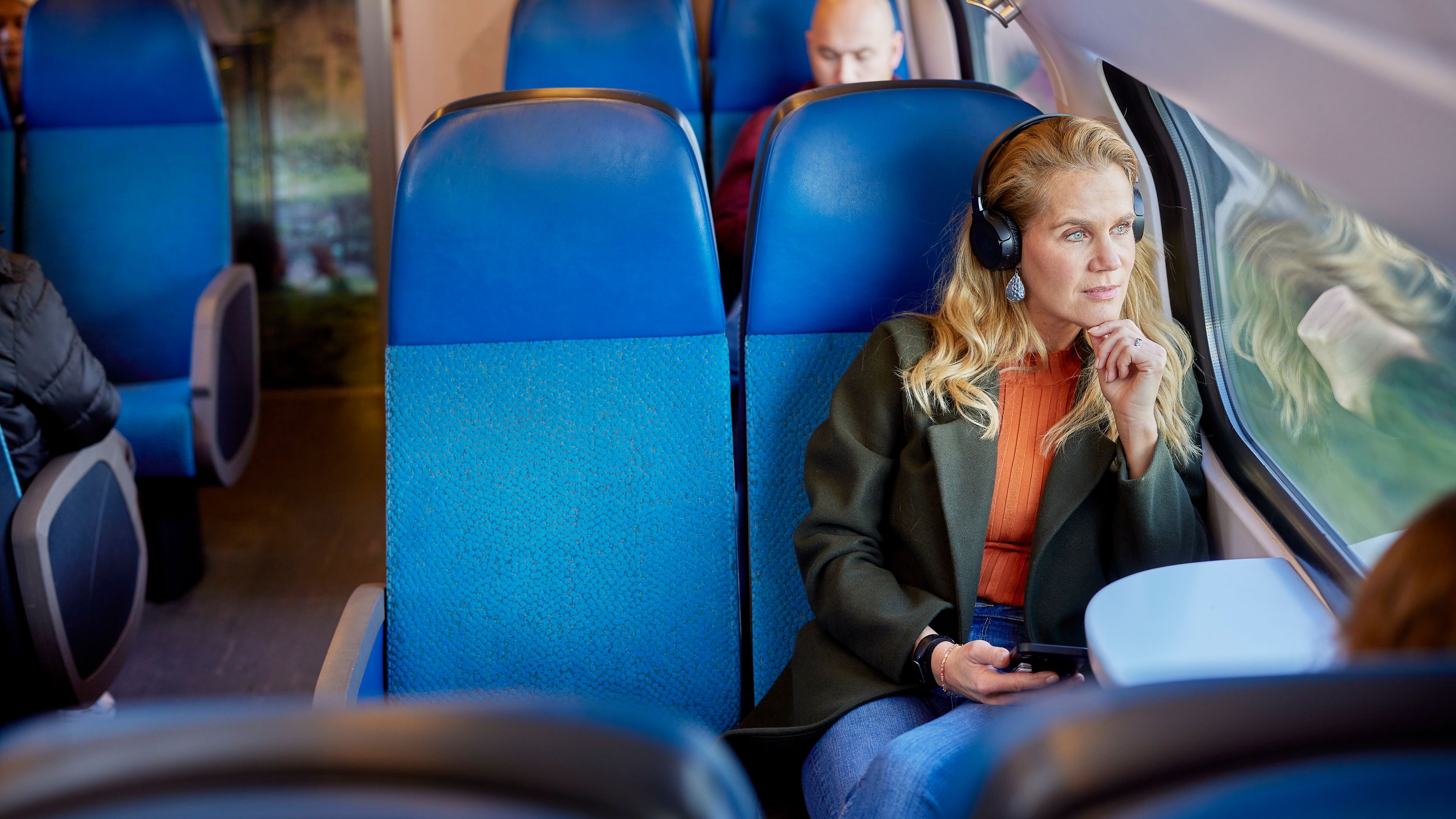 Vrouw die met een koptelefoon in de trein zit