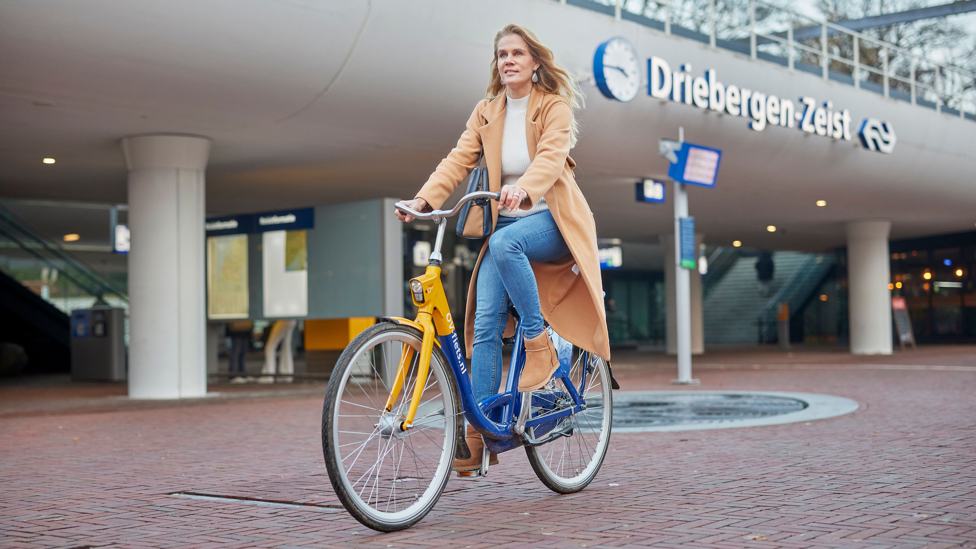 Een vrouw fietst op een OV-fiets weg van een treinstation.