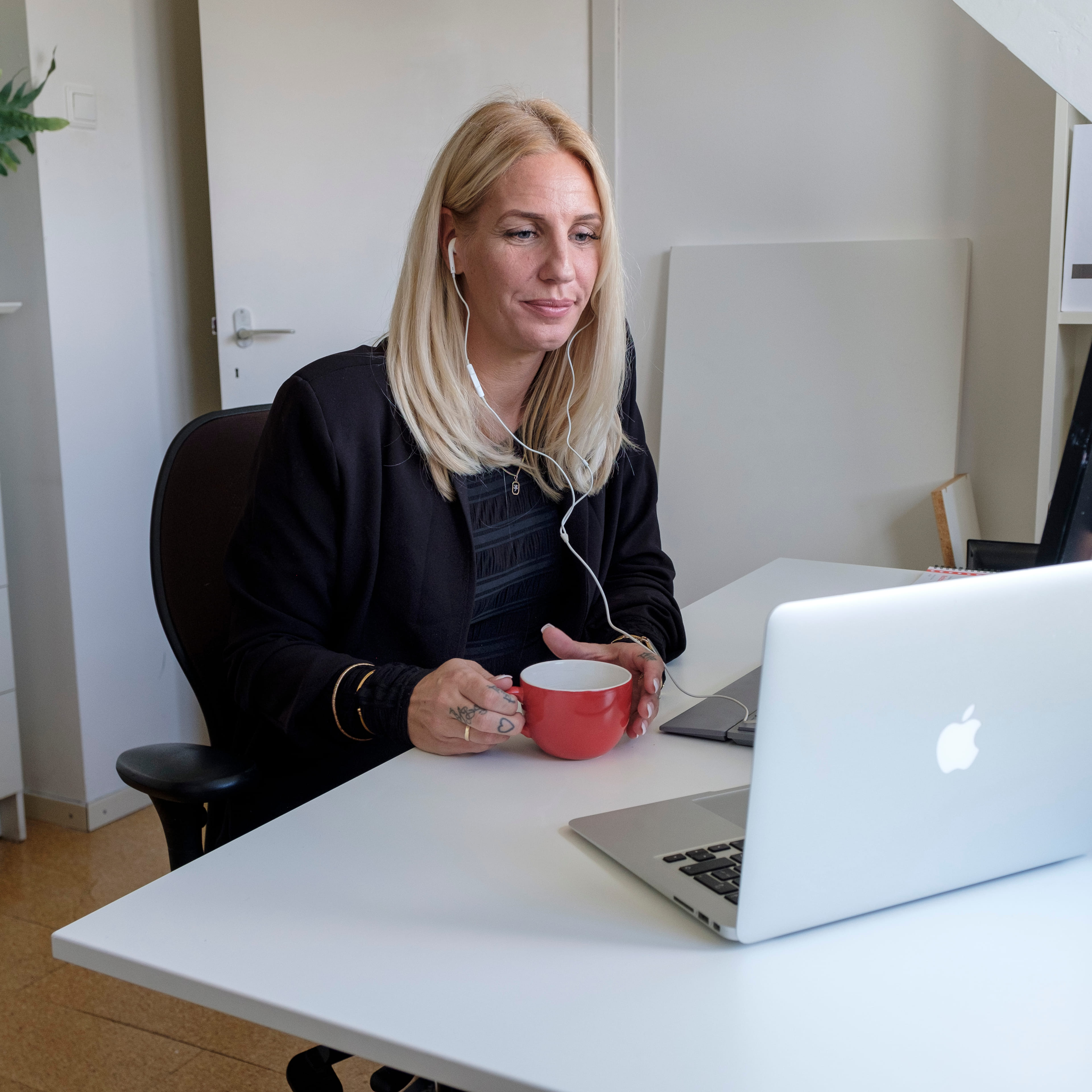Een vrouw zit met een kop koffie thuis aan tafel achter een laptop.