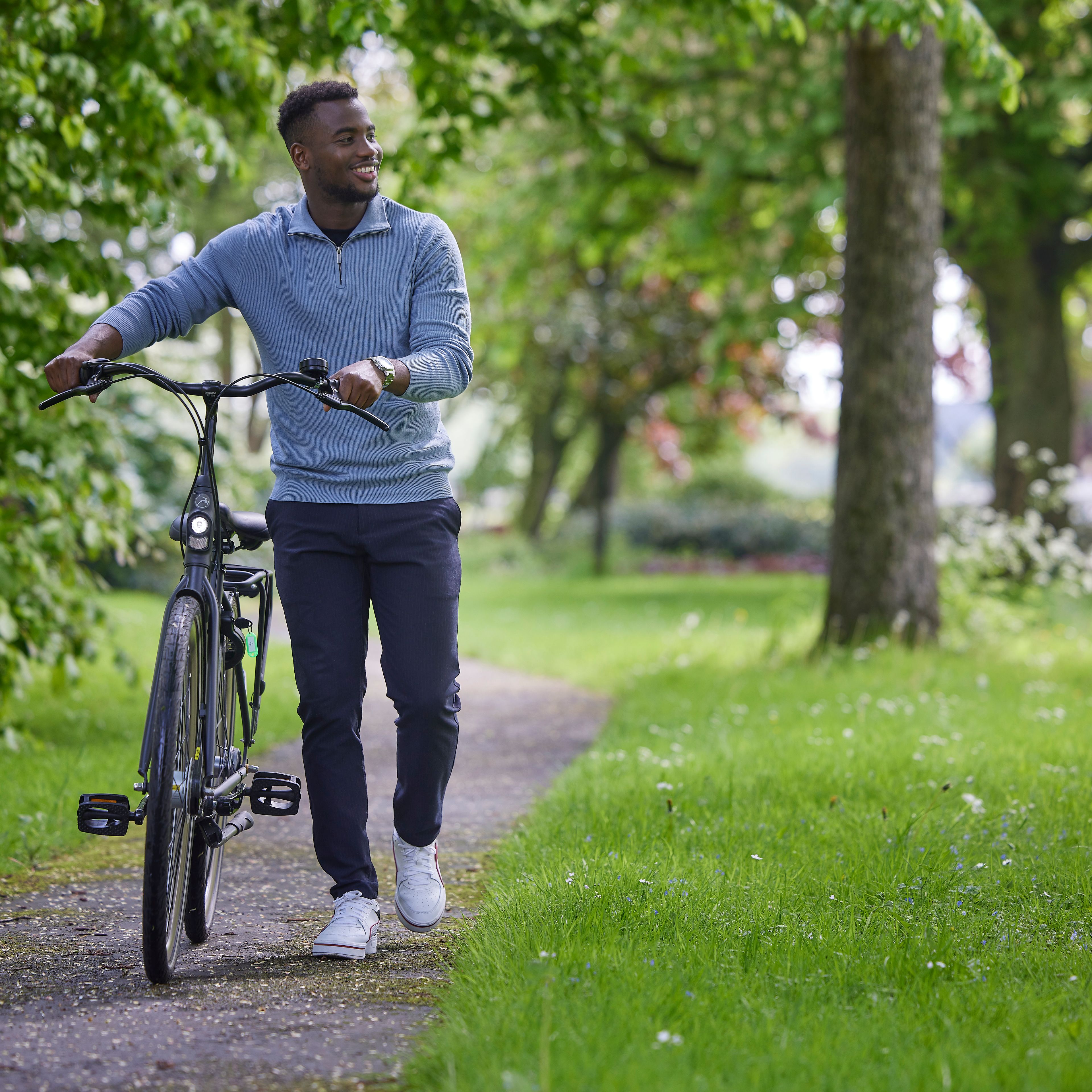 Man loopt met zijn fiets aan de hand door een park.