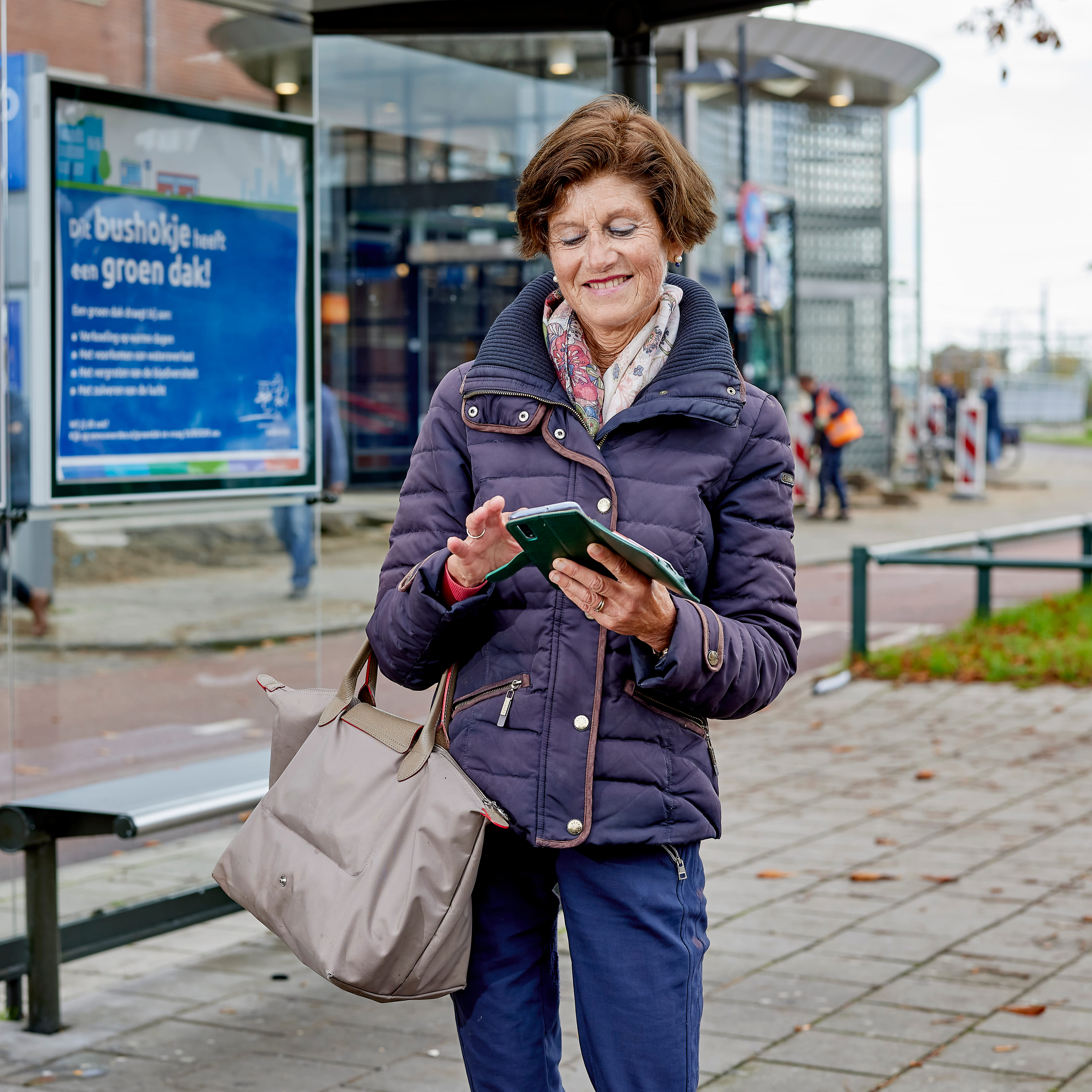Vrouw die bij de bushalte op haar telefoon kijkt