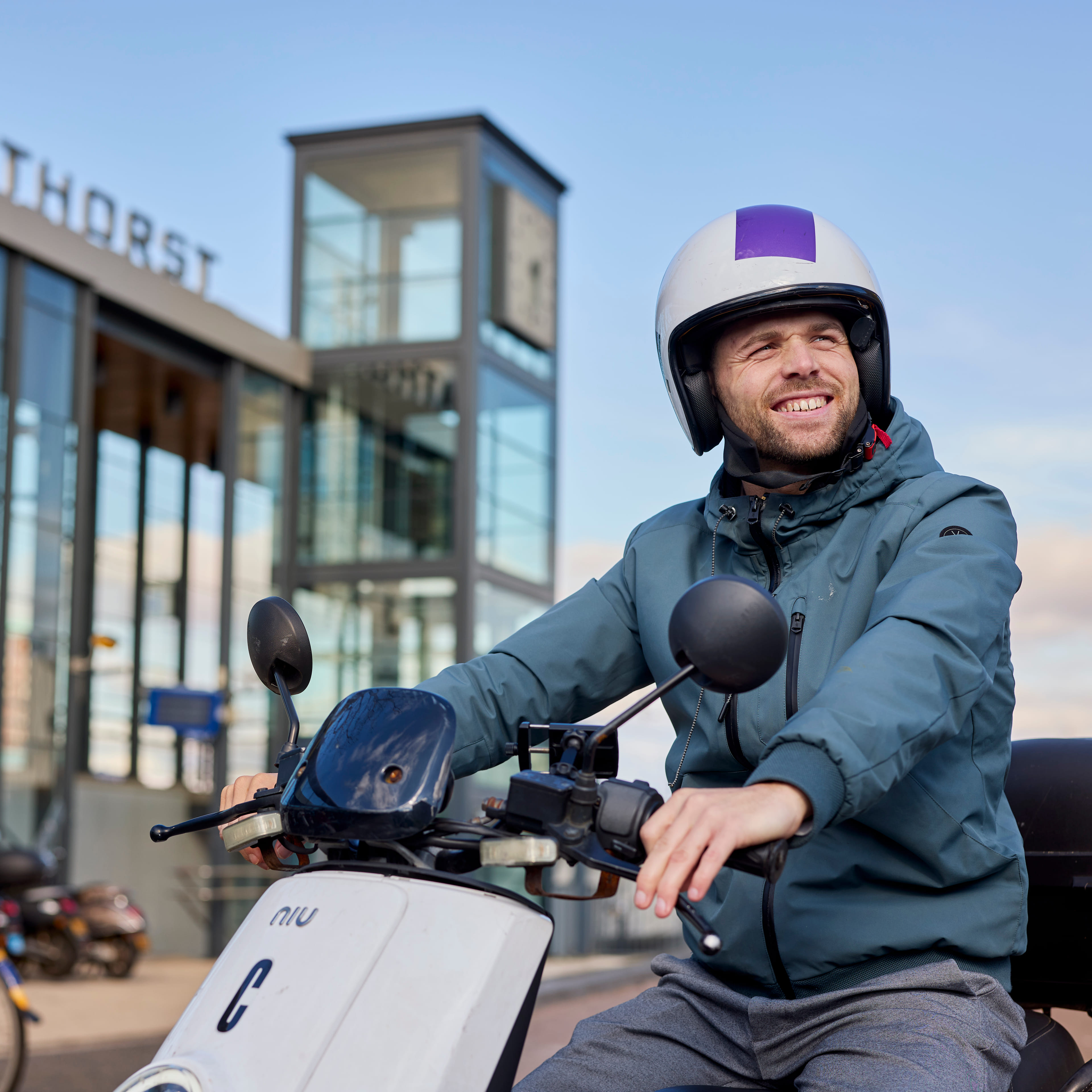 Je ziet een man op een check deelscooter zitten. Hij staat voor station Amersfoort Vathorst