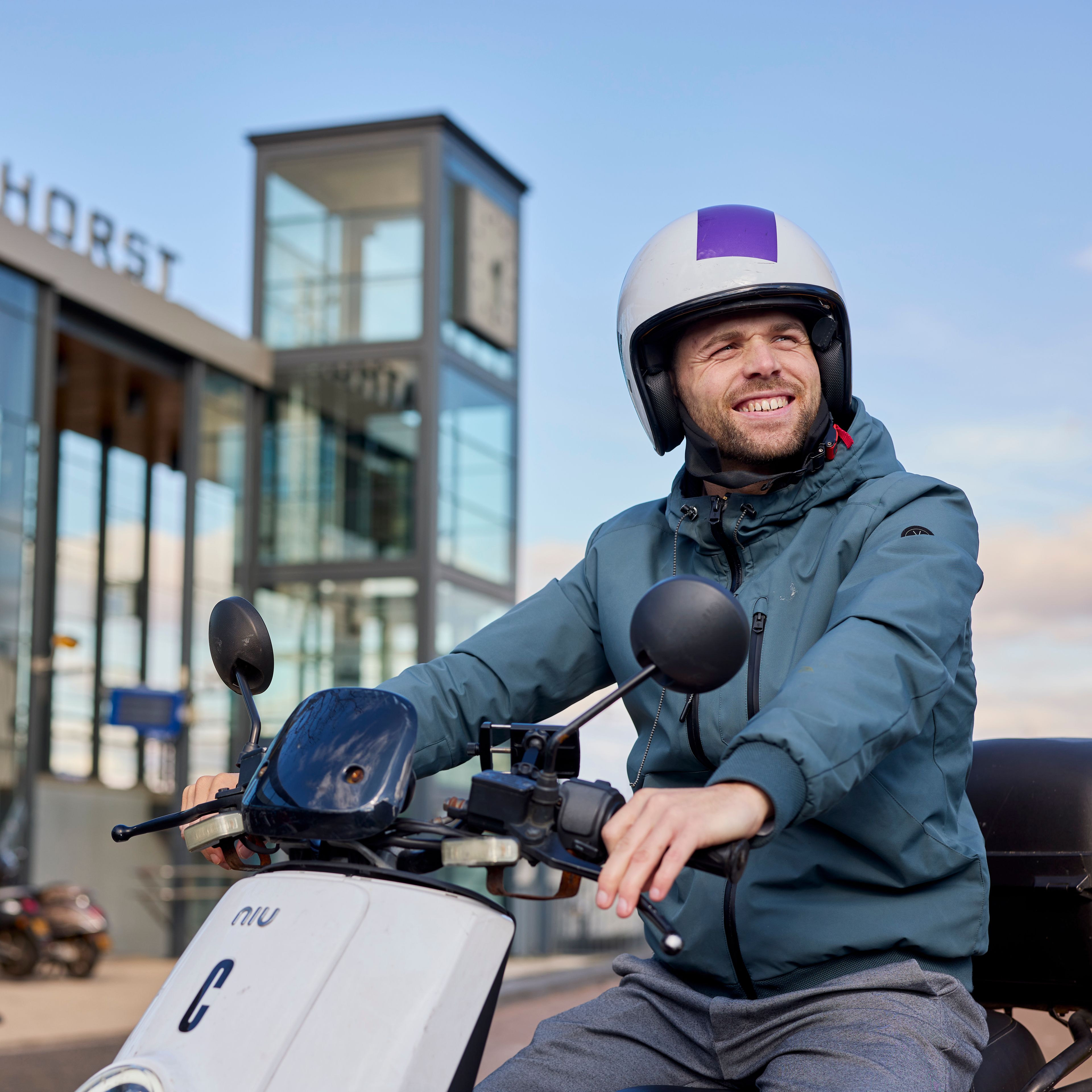 Je ziet een man op een check deelscooter zitten. Hij staat voor station Amersfoort Vathorst