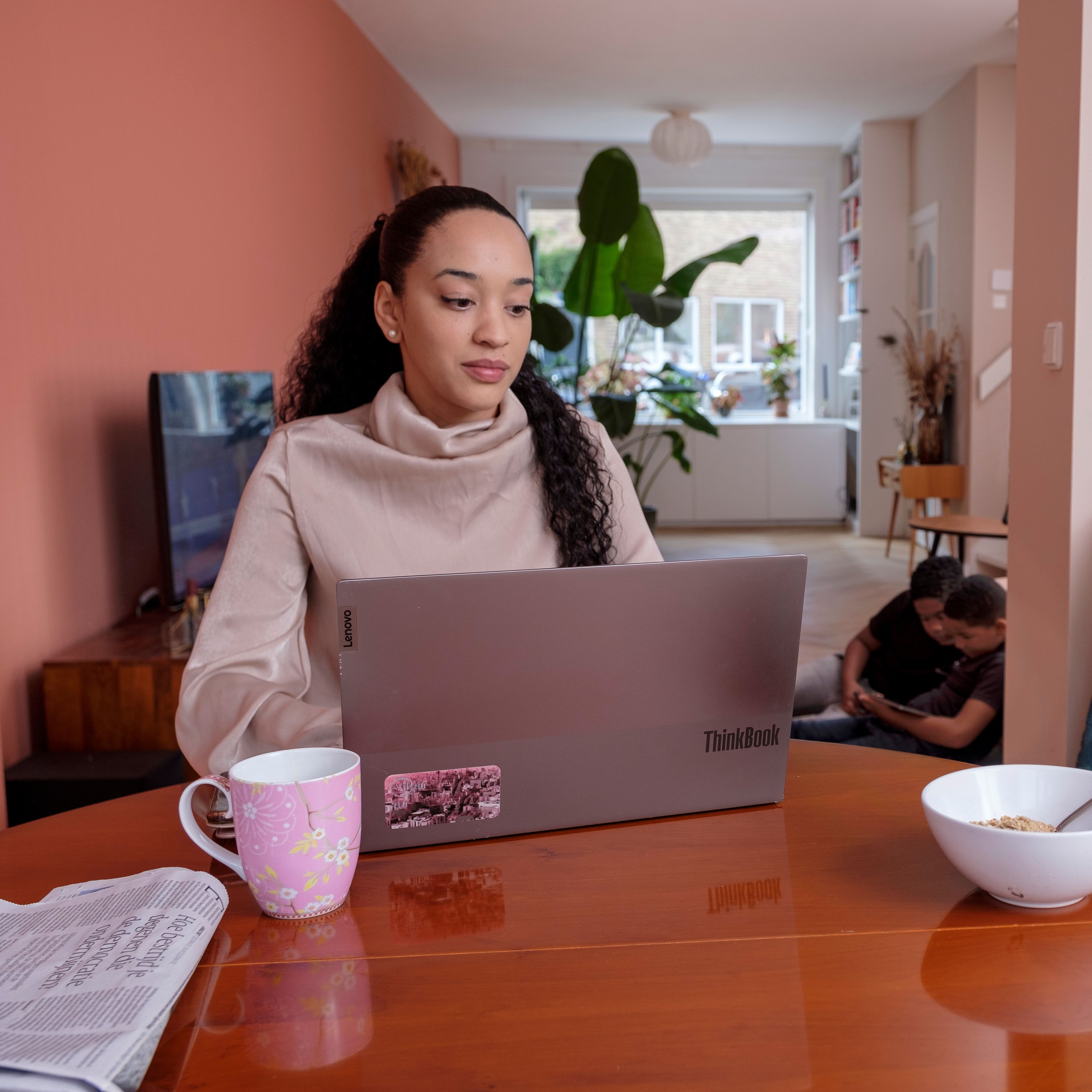 Een vrouw zit aan tafel, thuis achter een laptop.