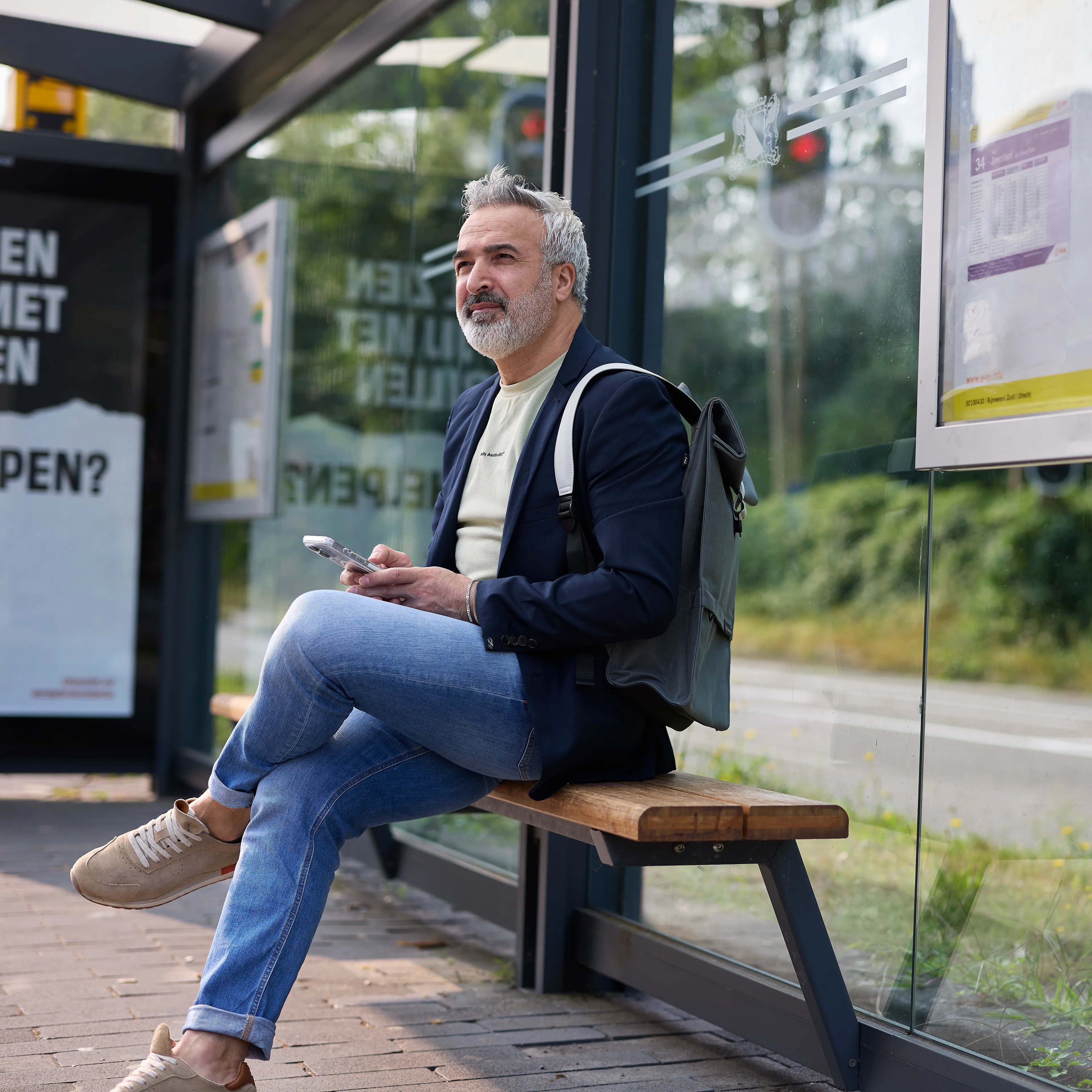 Man wacht zittend op de bus bij een bushalte