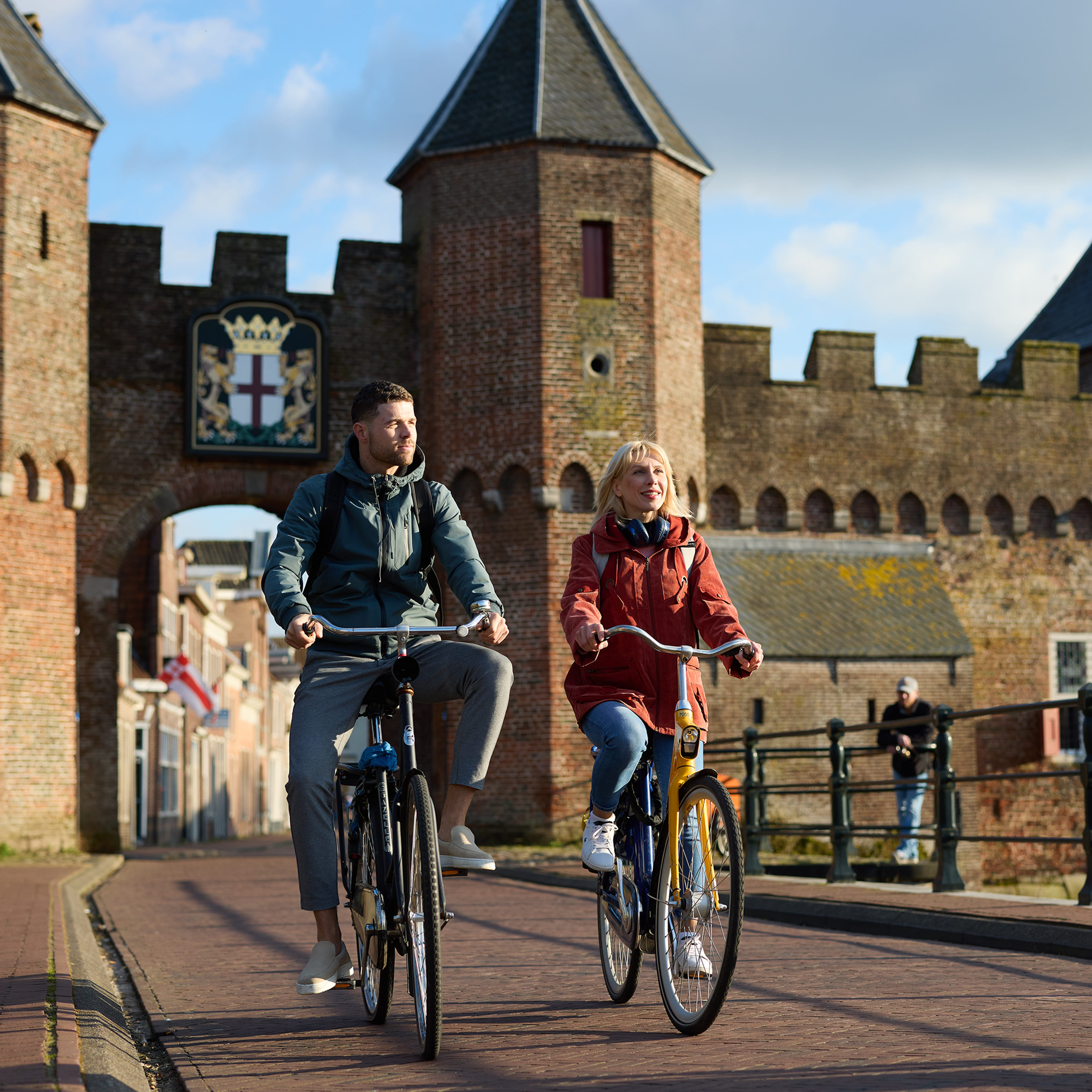 Je ziet een jongvolwassen vrouw en een jongvolwassen man samen door de stadspoort van Amersfoort centrum fietsen op een ov-fiets en een eigen fiets.