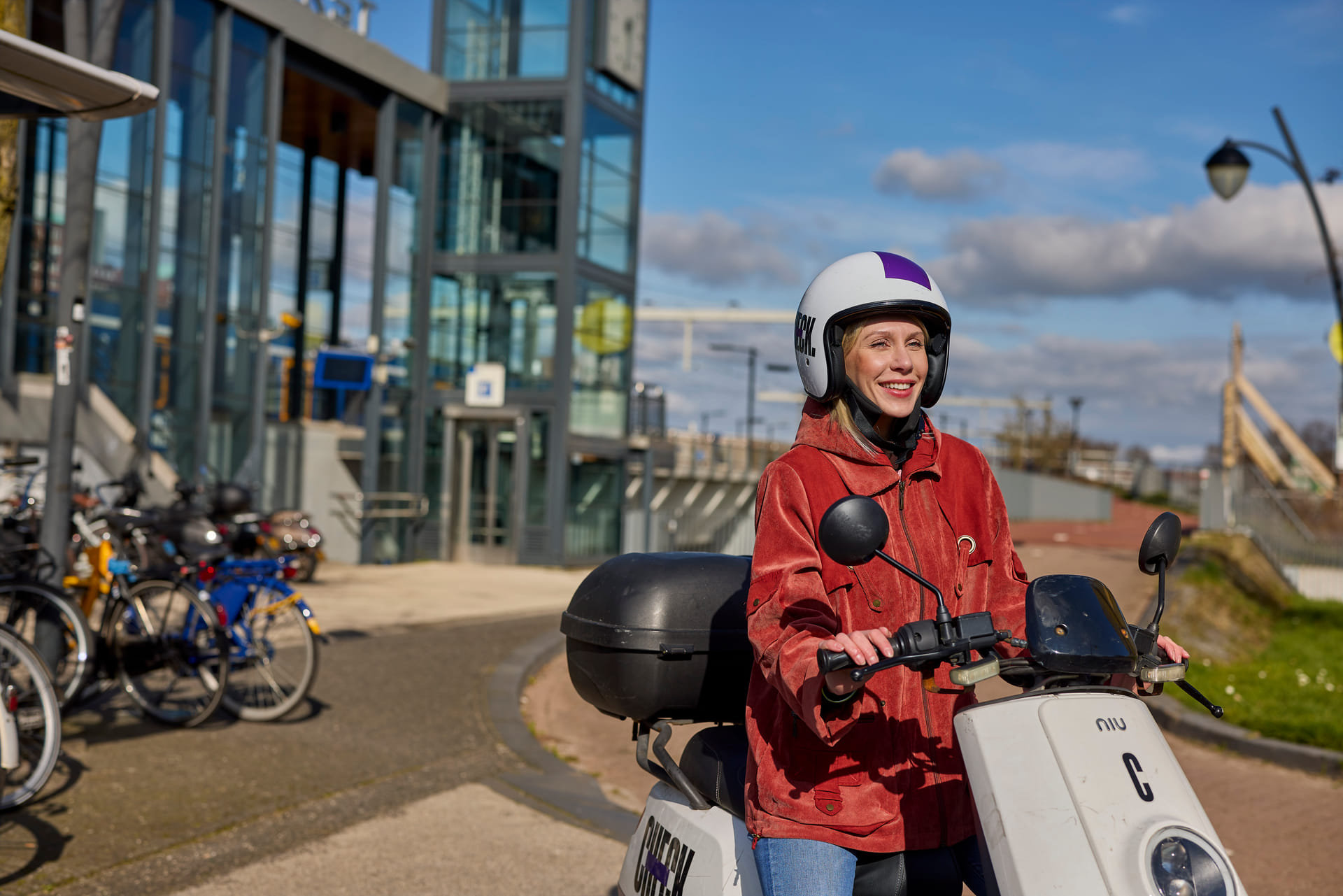 Je ziet een dame op een check deelscooter zitten. Ze staat voor station Amersfoort Vathorst