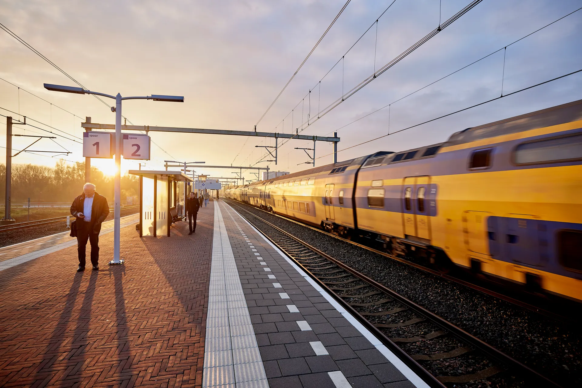 Een perron bij zonsondergang met een voorbij razende trein