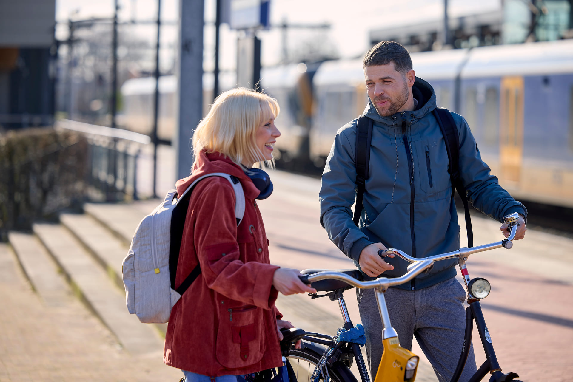 Je ziet een man en vrouw met elkaar lachen. Ze hebben beiden een fiets vast. Ze staan op station Amersfoort Vathorst.