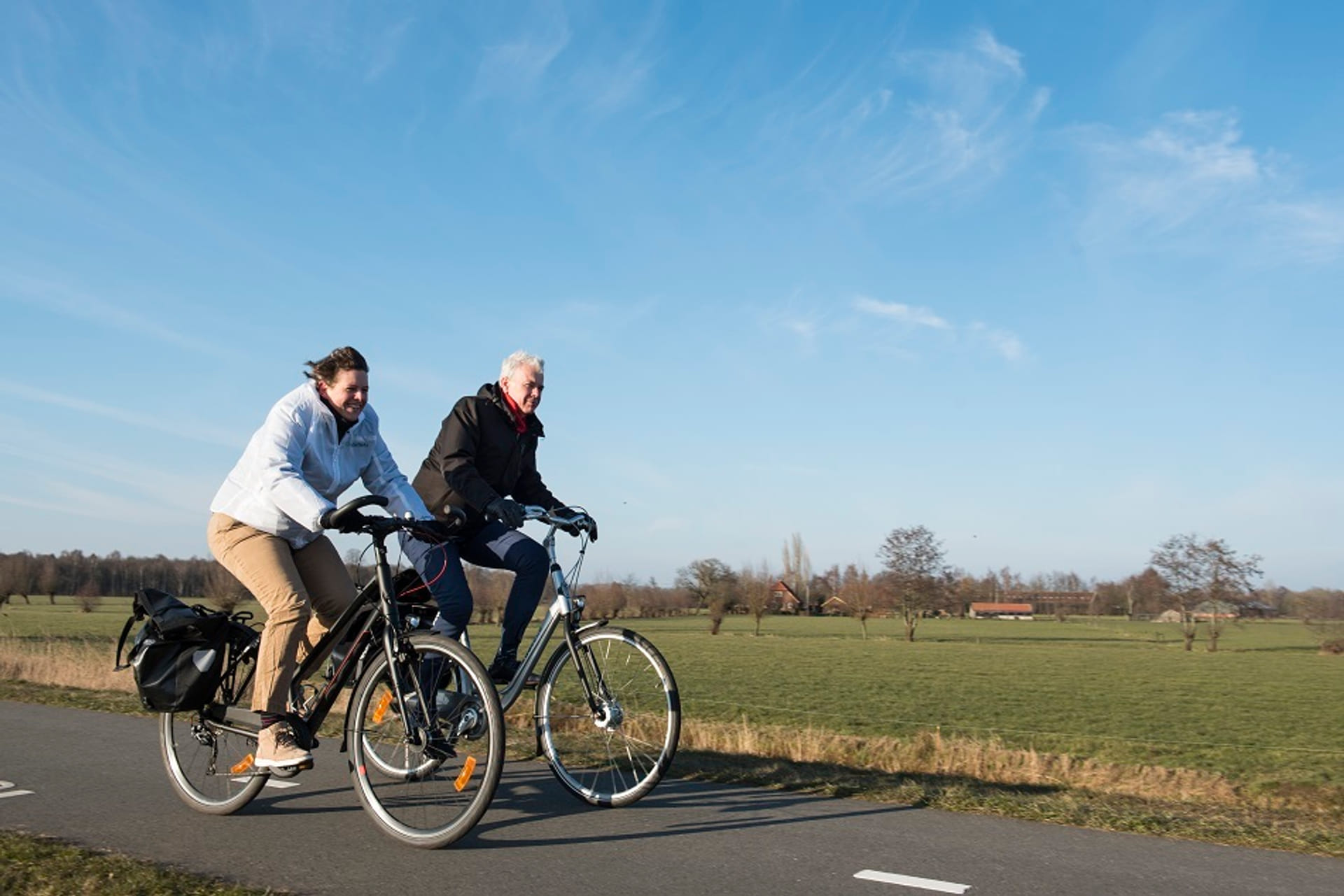 Man en vrouw fietsen samen door de weilanden.