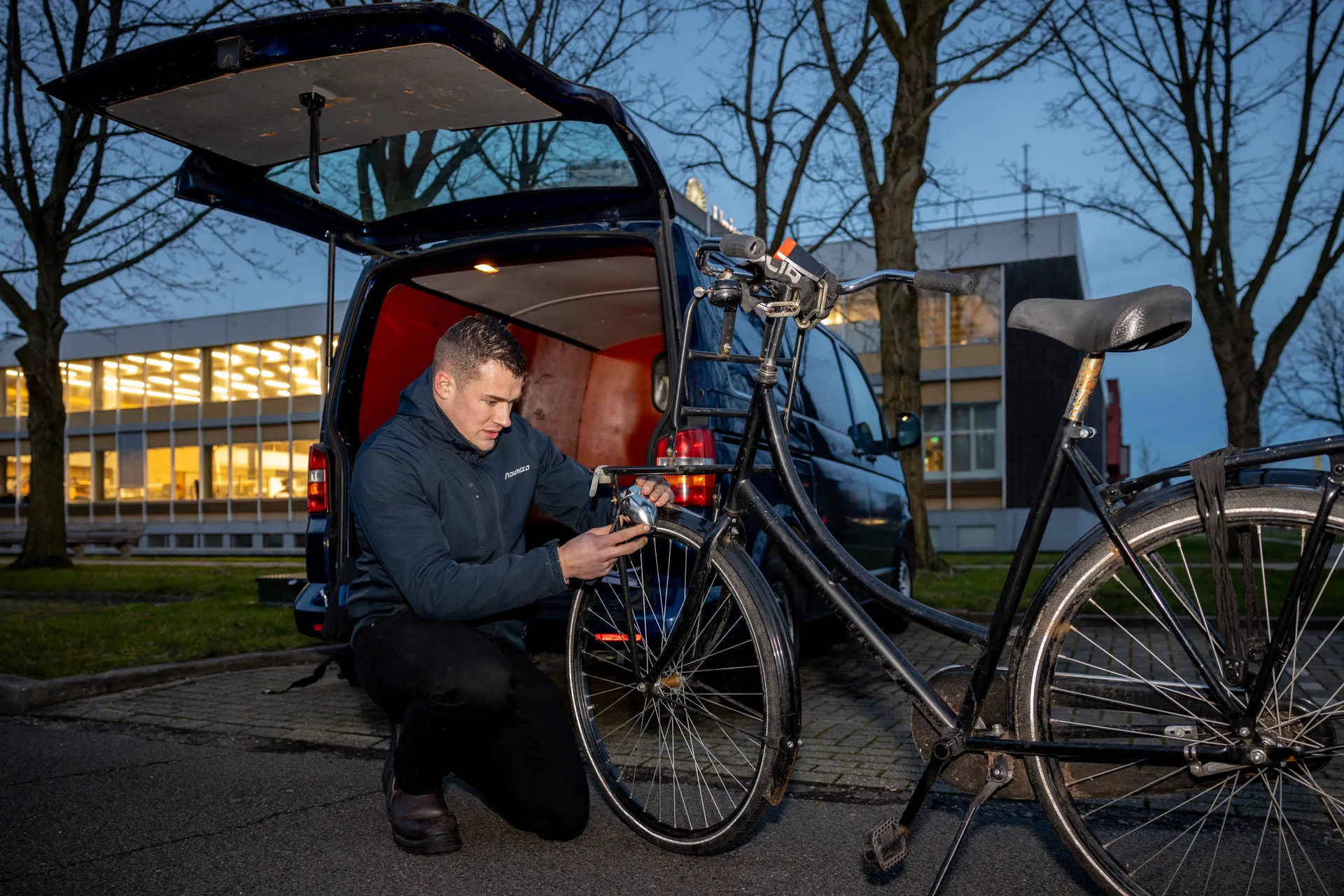 Een fietsenmaker vervangt een fietslichtje buiten in de schemer.