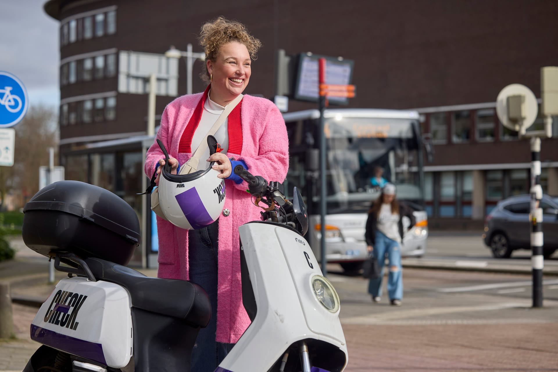 Een mevrouw die de helm van een Check deelscooter gaat opzetten. Er staat een check deelscooter voor haar.