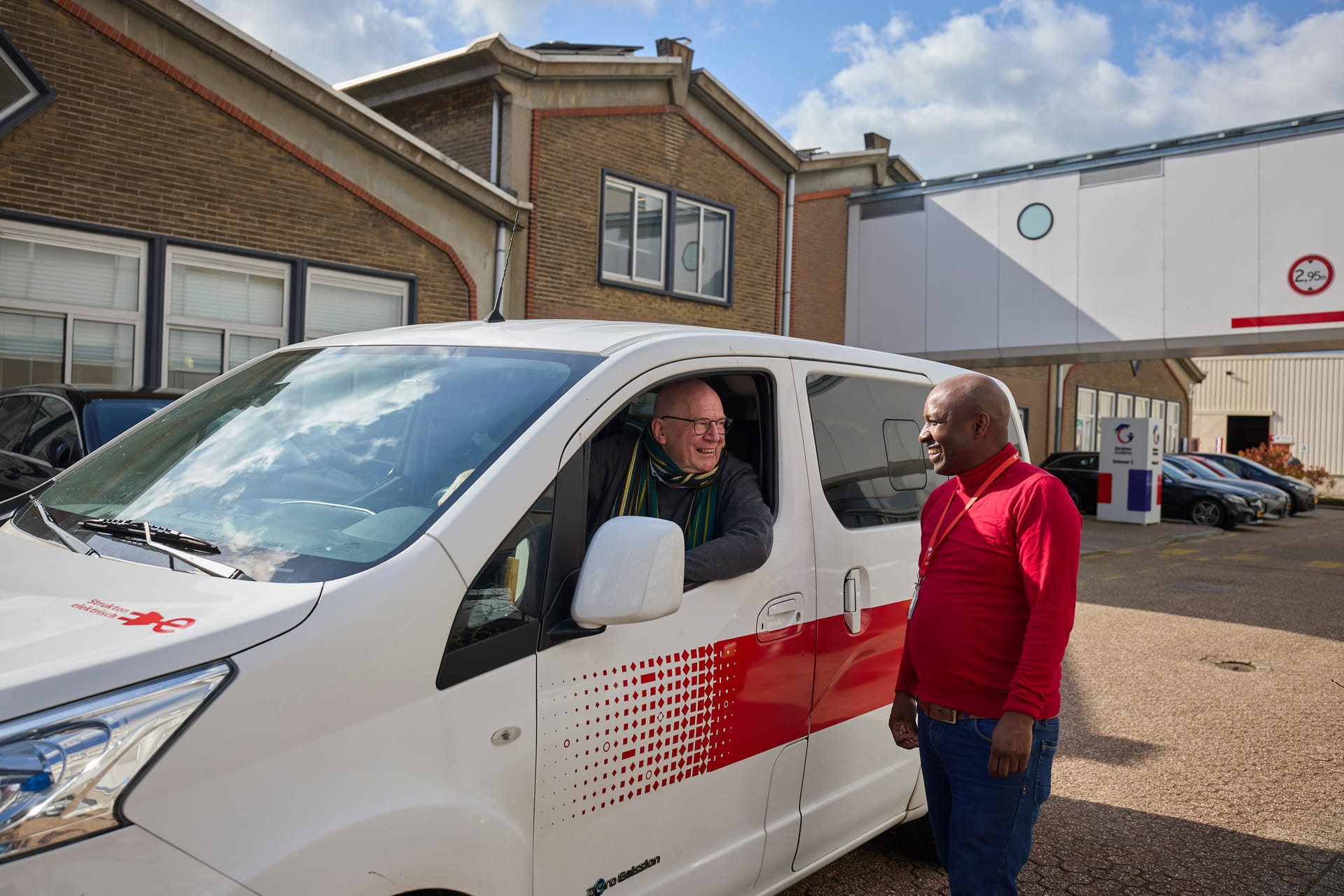 Je ziet een medewerker van Strukton bij een shuttlebus met chauffeur staan.