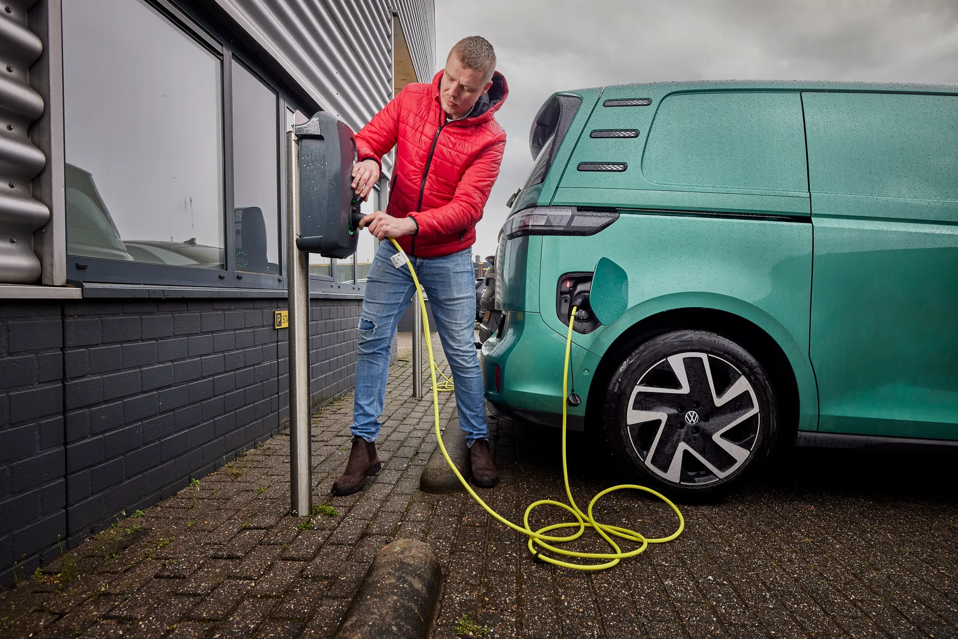 Man staat bij een laadpaal zijn elektrische bestelbus op te laden.