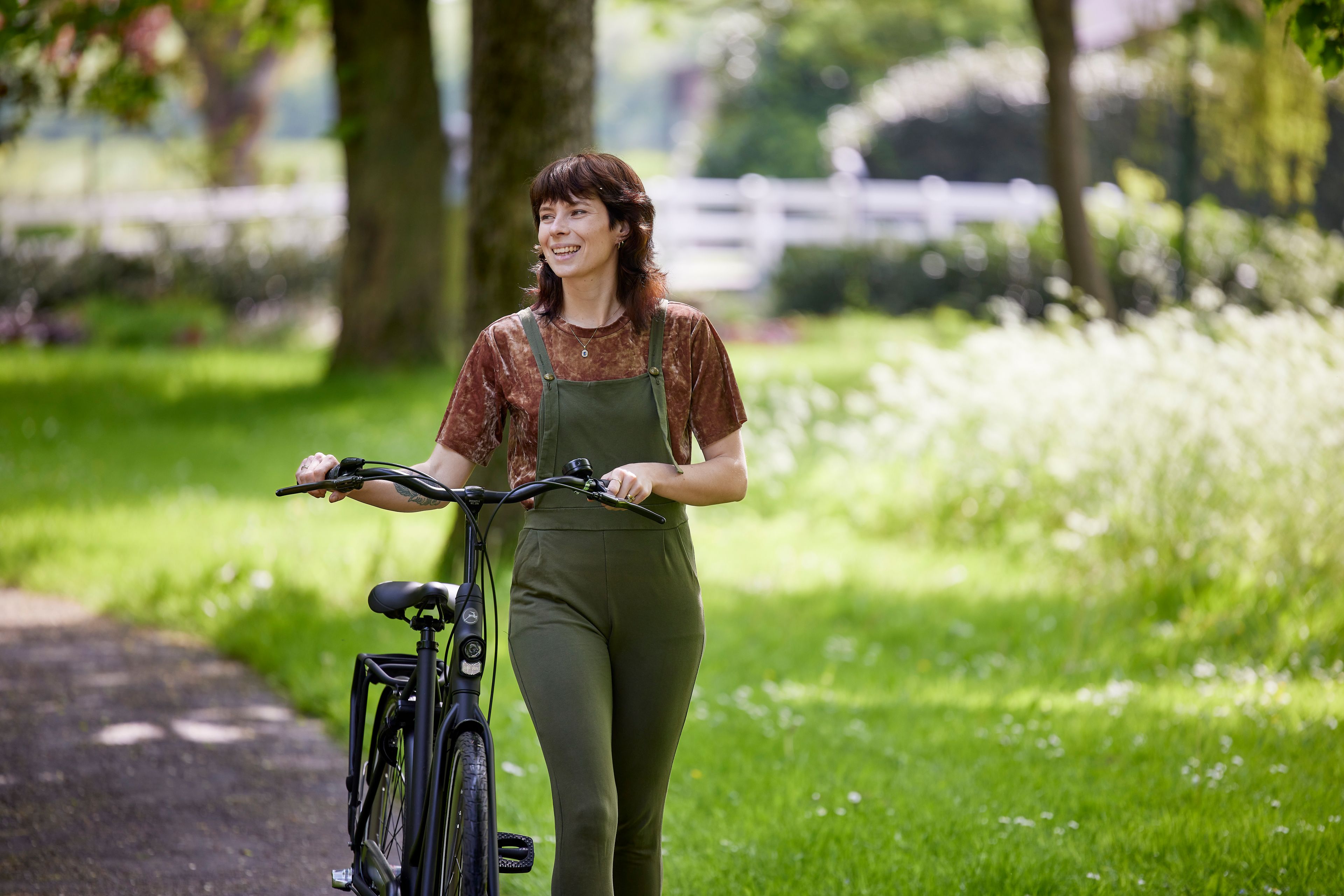 Vrouw loopt met haar fiets aan de hand door een park.