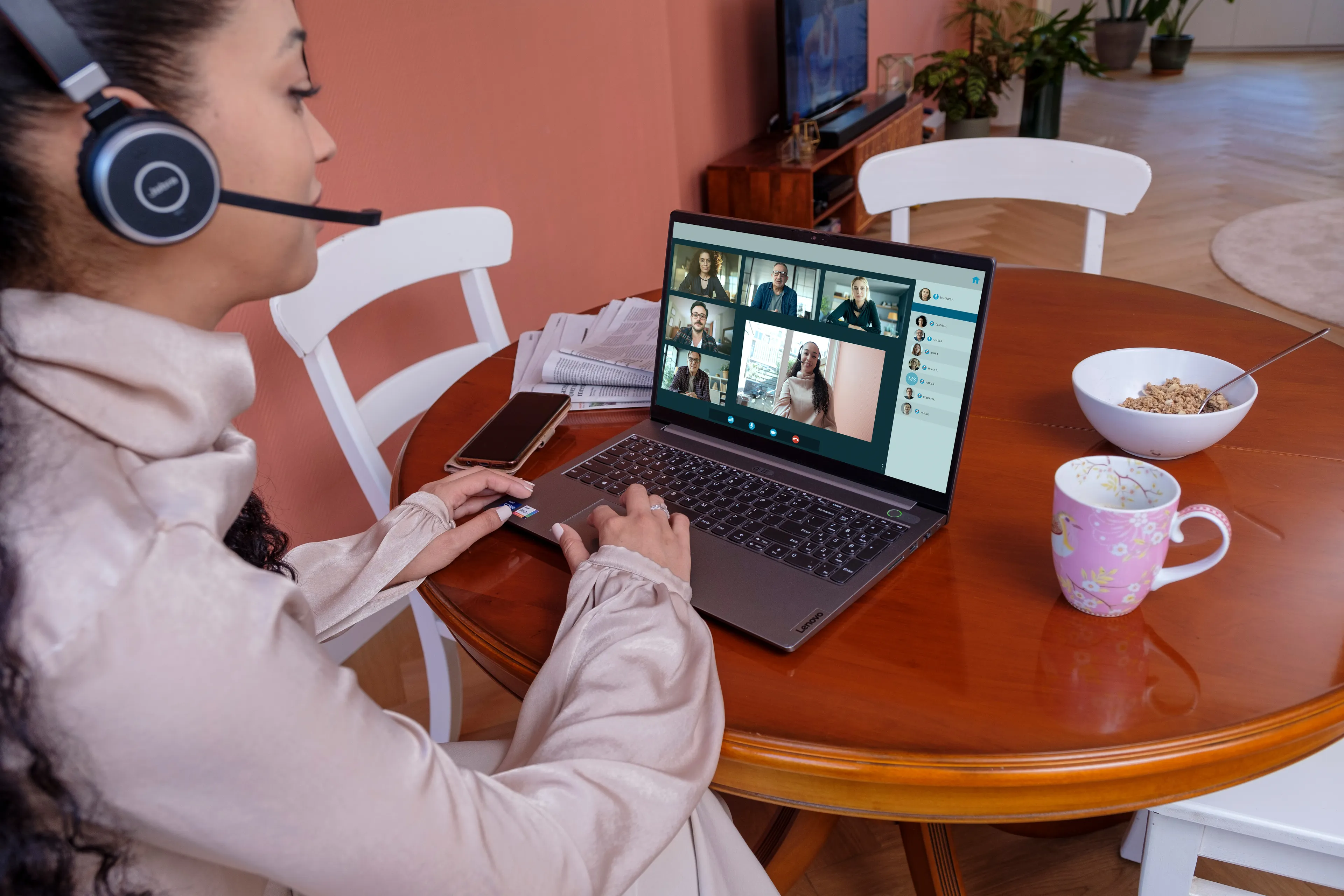 Een vrouw zit met een koptelefoon op thuis achter een laptop. Op het scherm zien we een videocall.